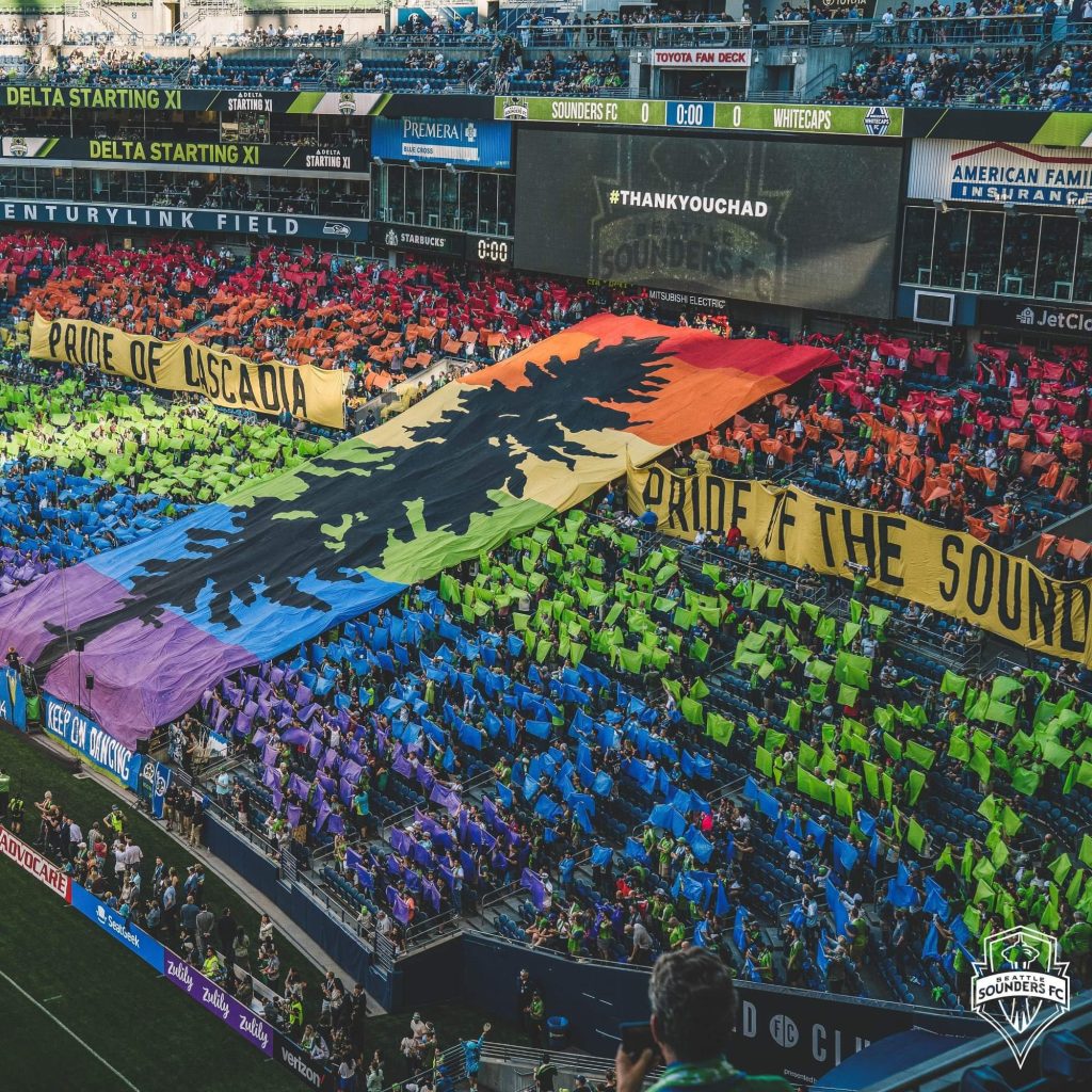 A giant Cascadia pride flag tifo raised across a packed stadium crowd.